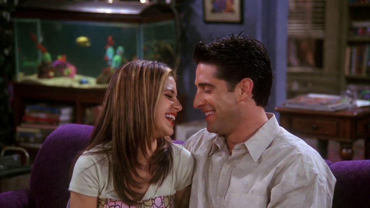 Monica and Chandler laughing together on the couch in Friends apartment, iconic Mondler funny couple moment